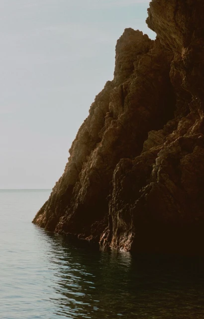 A scenic view of a rocky cliffside meeting the ocean under a clear sky, creating a serene seascape with natural textures and earthy tones.