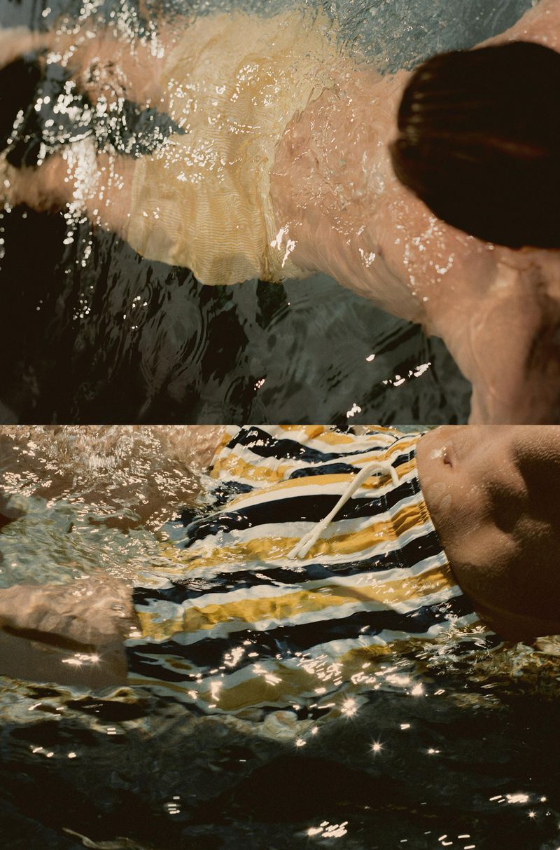 Person in a swimming pool wearing striped swim trunks with white drawstring, water rippling, and sunny, creating dappled light.