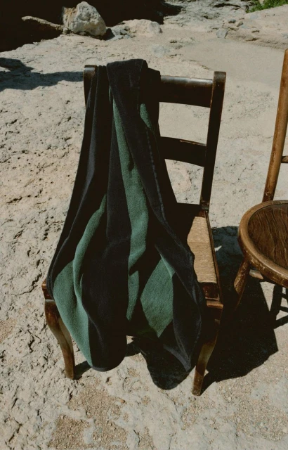 Green and black striped fabric draped on a wooden chair outdoors in natural light, next to a second empty chair on textured ground.
