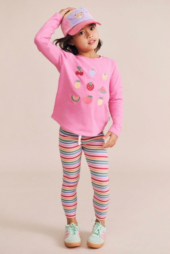 Child model wearing a pink long-sleeve graphic top and multi-colored striped leggings against a plain light background