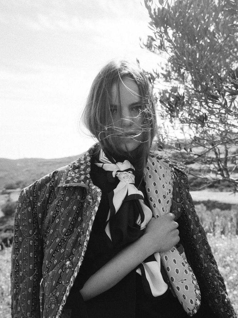 Model in patterned jacket and silk scarf outdoors in a black and white portrait for Celine Fall 2026 campaign.