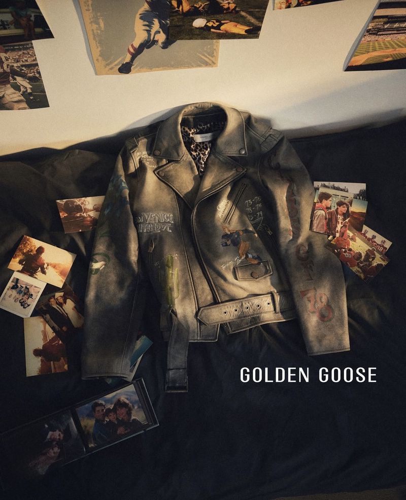 Distressed grey leather biker jacket with painted graphics laid out on a dark bed surrounded by scattered printed photographs.