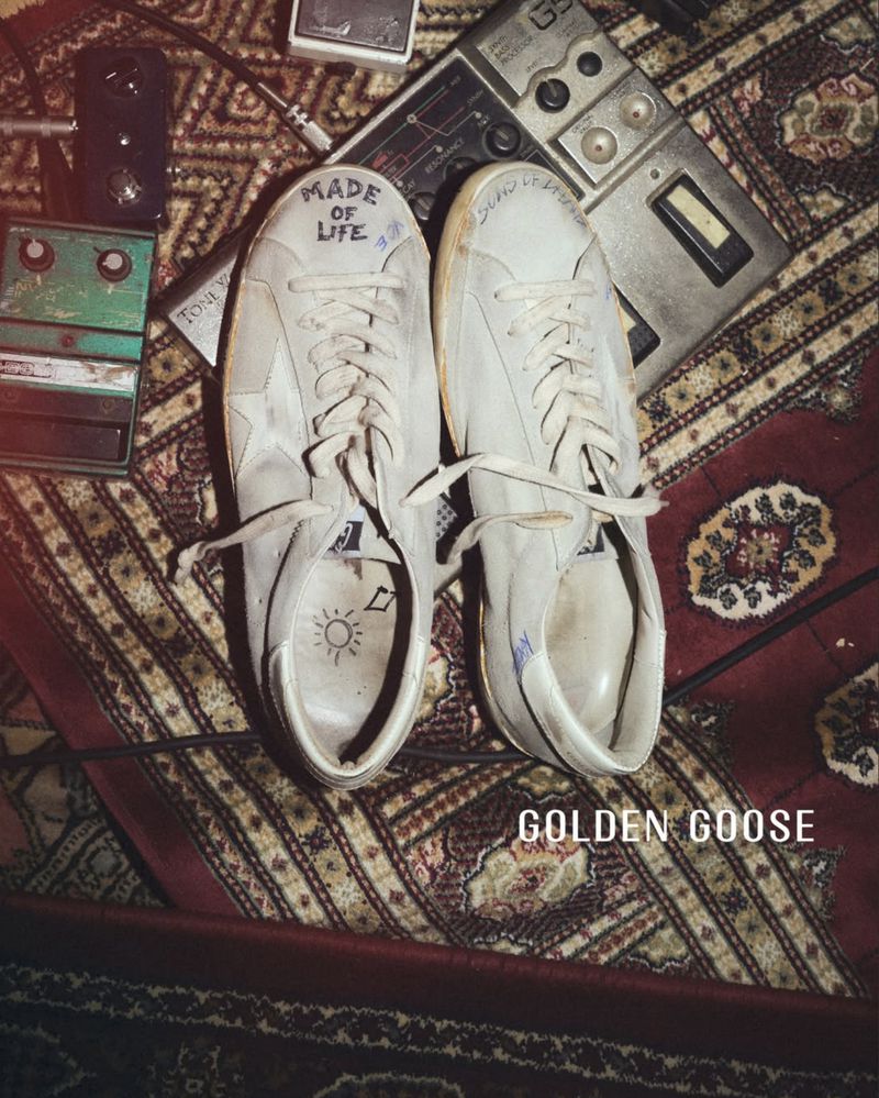 Distressed white sneakers customized with handwritten text on an ornate patterned rug alongside vintage audio pedals.