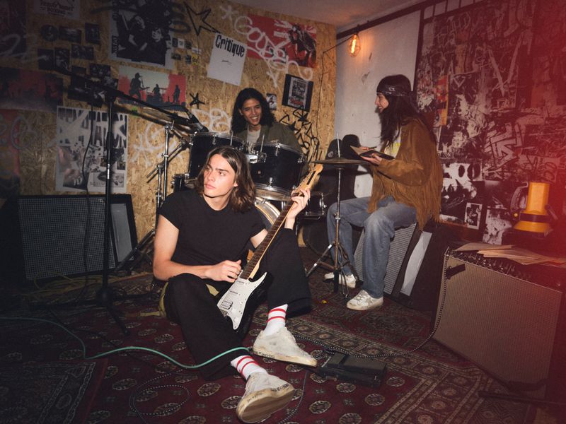 Three young musicians in a rehearsal room with a drum kit and guitar for Golden Goose campaign