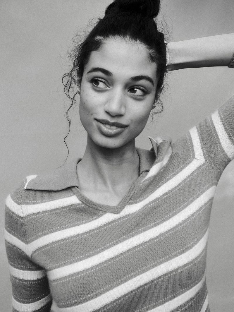Black and white portrait of Malika El Maslouhi wearing a striped collared knit polo top with one arm raised behind her head.
