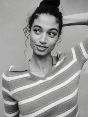 Black and white portrait of Malika El Maslouhi wearing a striped collared knit polo top with one arm raised behind her head.