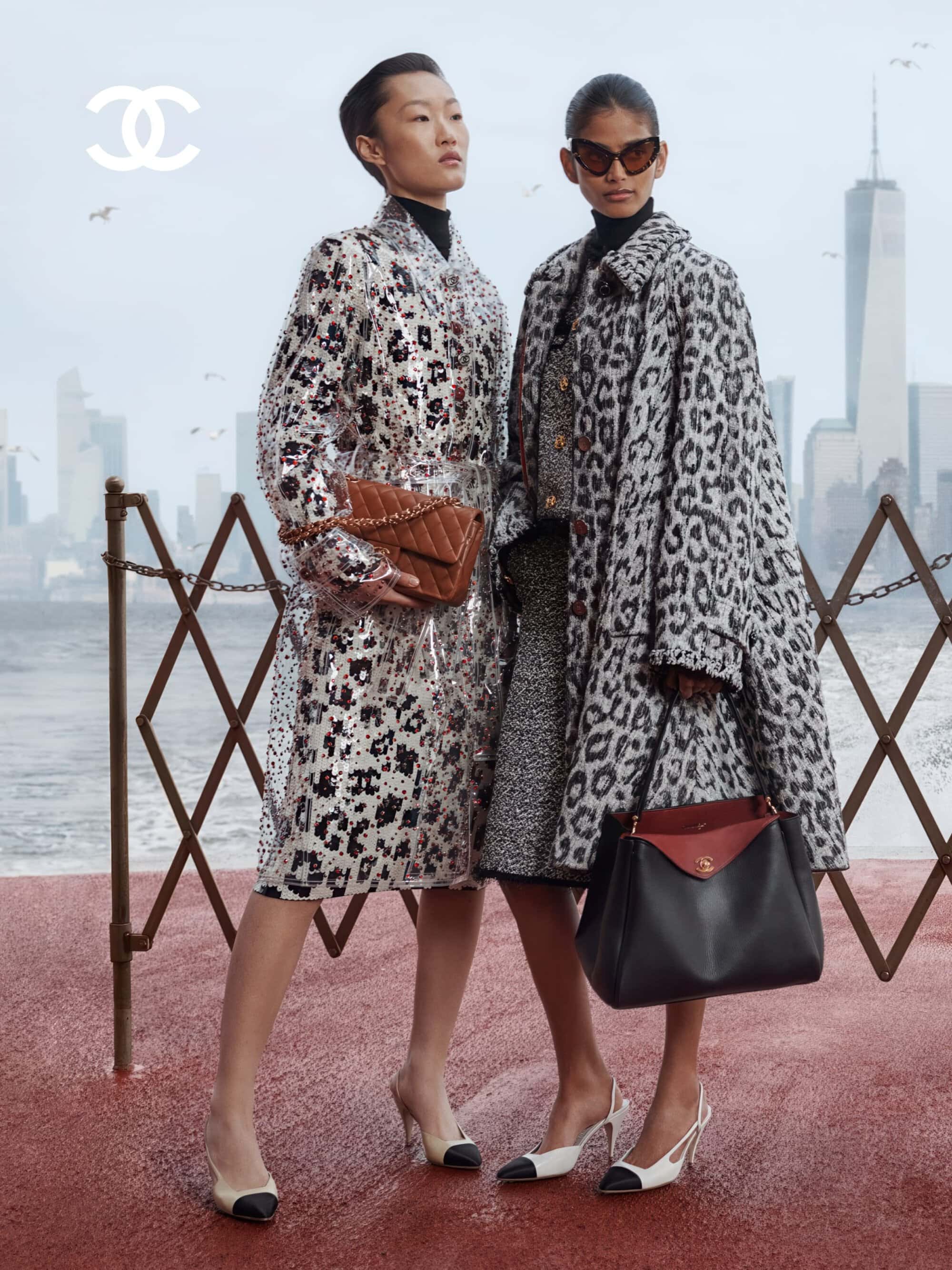Two fashion models posing in patterned coats with Chanel leather handbags against a misty waterfront city skyline.