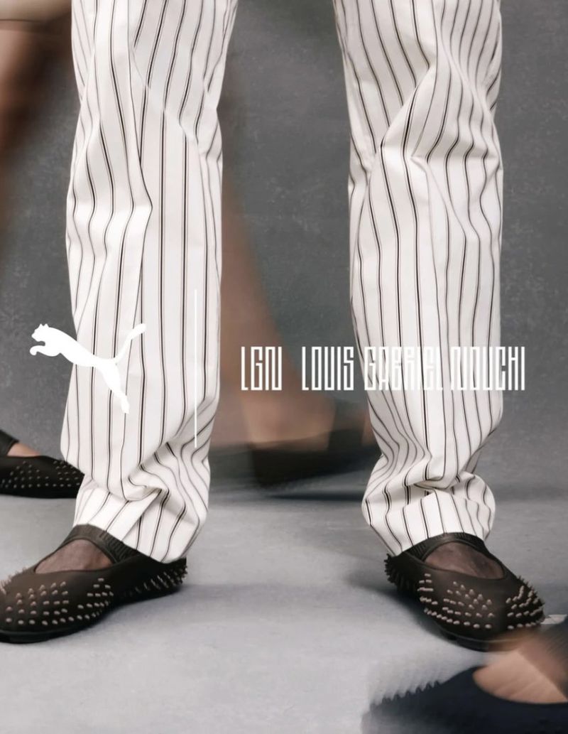 Close up of a person wearing black and white striped pants and black studded shoes, featuring a Puma logo and LGNU Louis Gabriel Nouchi text.