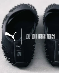 Close-up of black spiked Puma x LGN Louis Gabriel Nouchi Mostro slip-on shoes placed on a smooth grey surface.