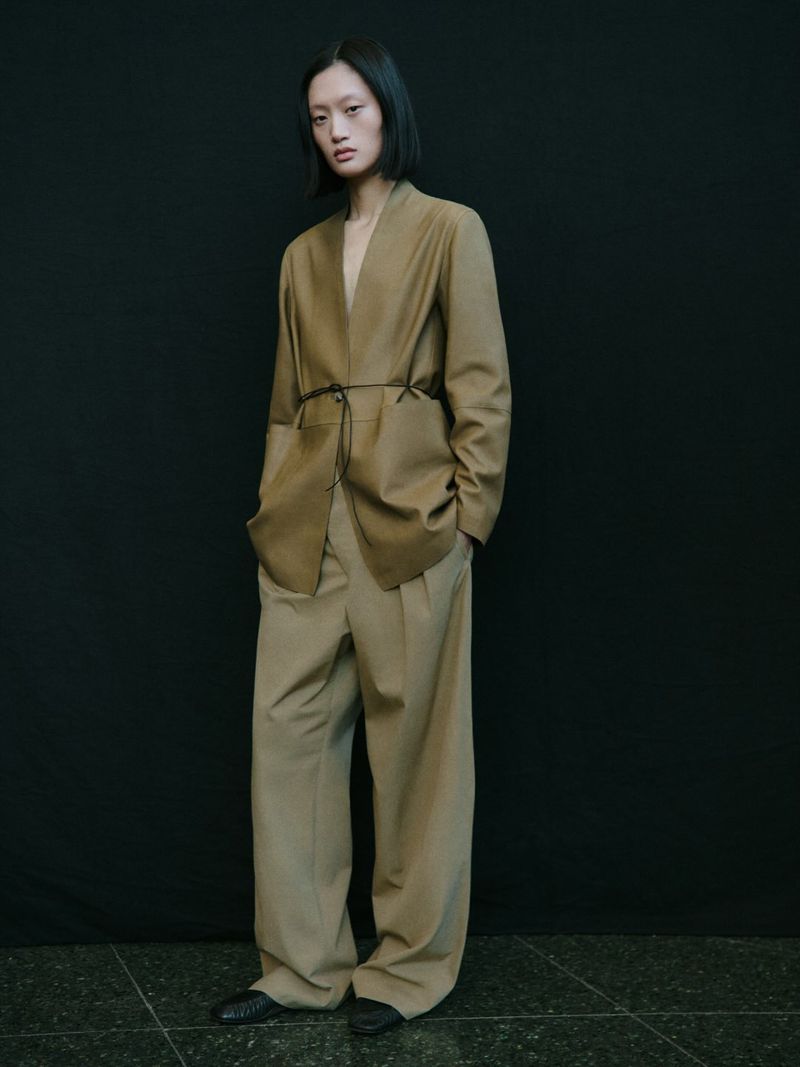 Model wearing a tan blazer and matching trousers standing against a dark seamless background for Massimo Dutti Studio