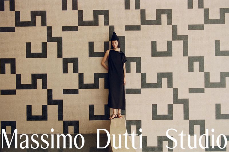 Model in a black midi dress and hat stands against a geometric pattern mosaic wall for Massimo Dutti Studio.