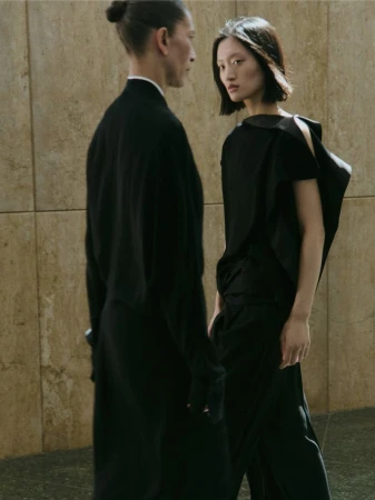 Yilan Hua in a draped black top alongside Liset Mitjan posing against a beige stone wall for Massimo Dutti Studio.