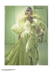 Maria Klaumann posing in an expansive pale lime green ruffled gown in a monochrome studio set with a vintage armchair.