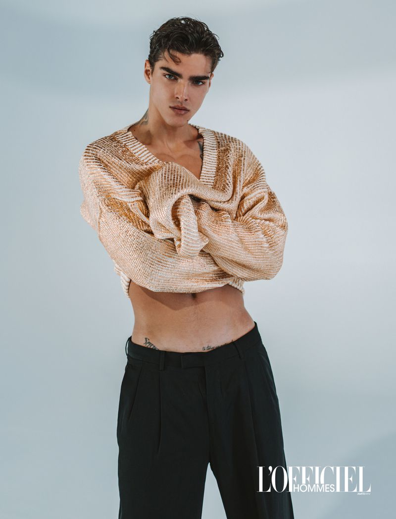 Model Simone Stravolo wearing a cropped beige knit sweater and black trousers in a studio editorial for L'Officiel Hommes Ukraine.