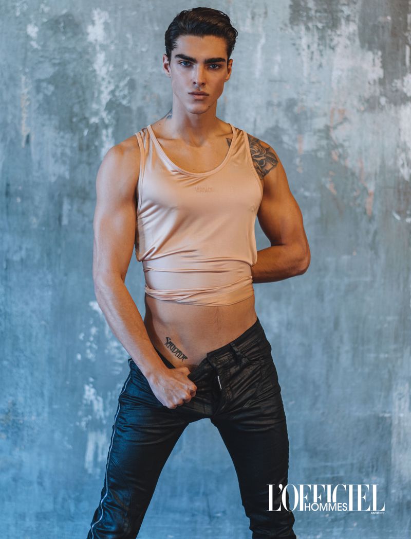 Model Simone Stravolo wearing a peach tank top and black pants against a textured blue-grey wall for L'Officiel Ukraine.