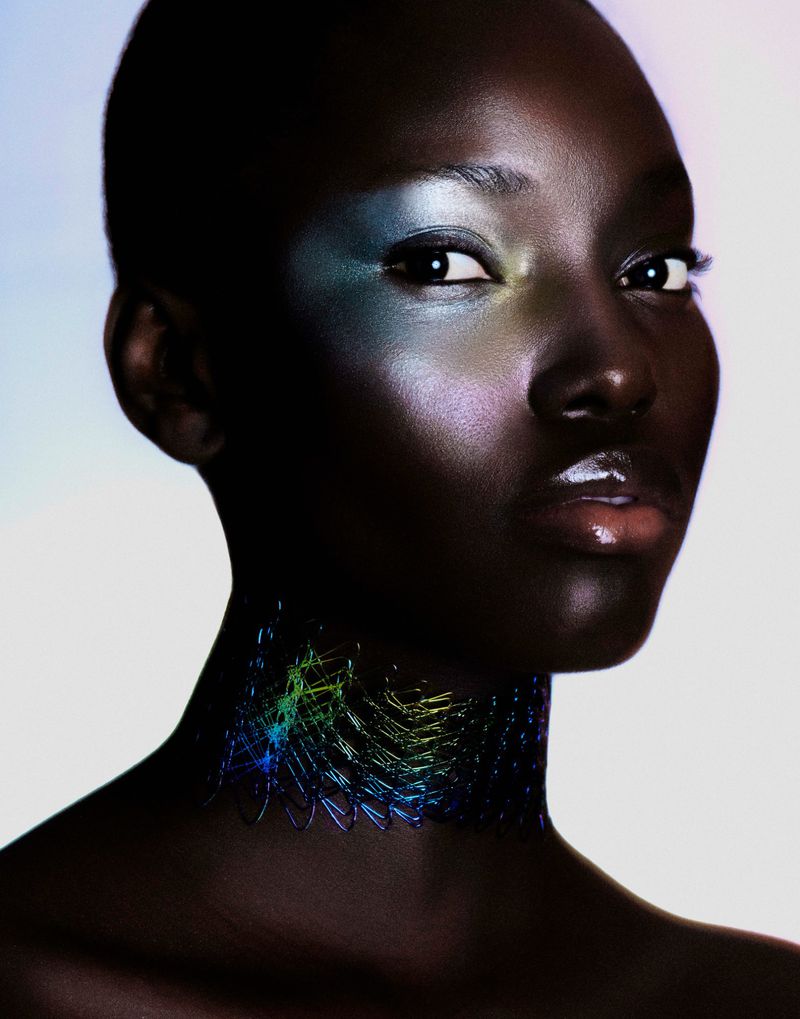 Close-up beauty portrait of a Black woman with iridescent eye makeup and an intricate glowing mesh choker necklace.