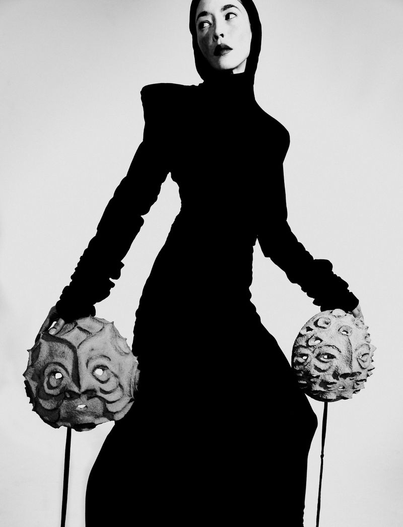 Model in black turtleneck dress holding two textured round face sculptures for Title Magazine