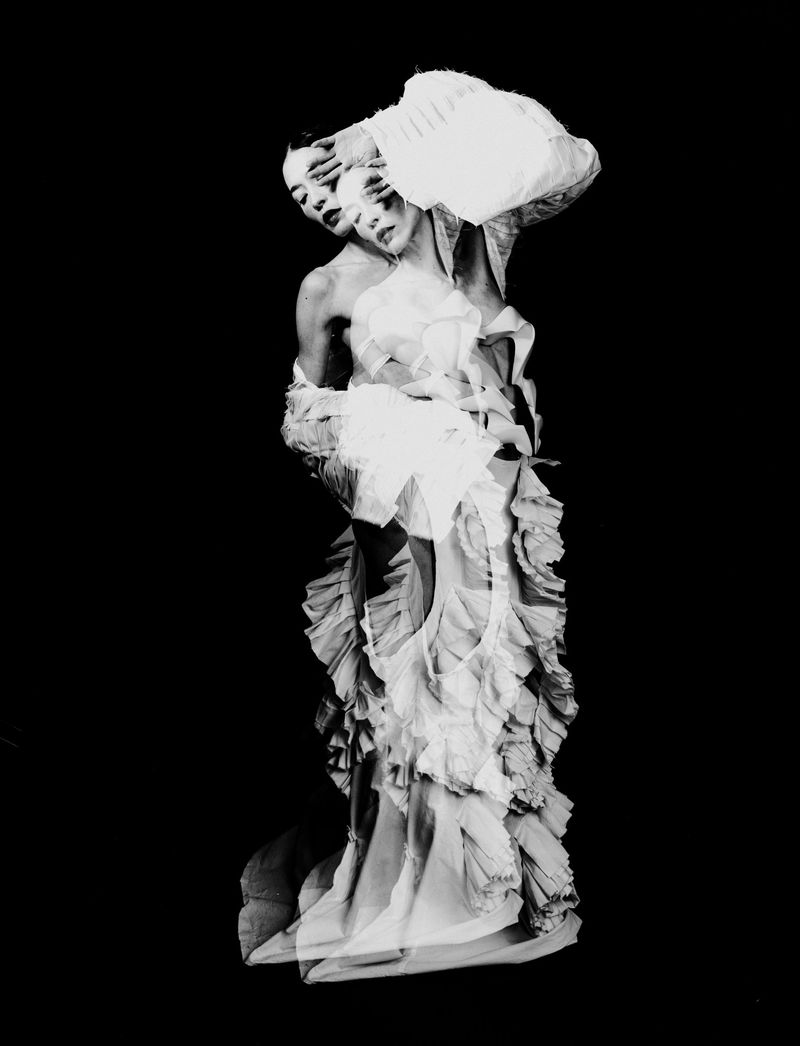 Black and white multiple exposure portrait of a woman in a textured ruffled gown posing against a solid black background.