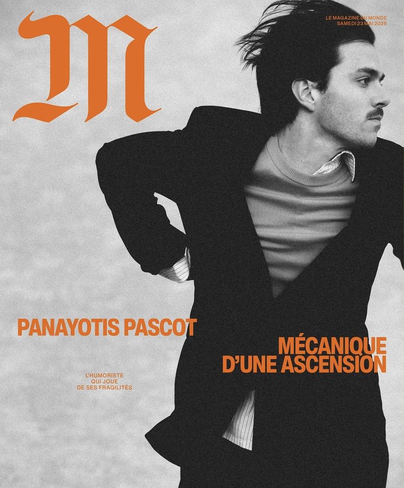 Magazine cover featuring a man wearing a black suit jacket and a grey shirt, set against a grey background with orange typography.