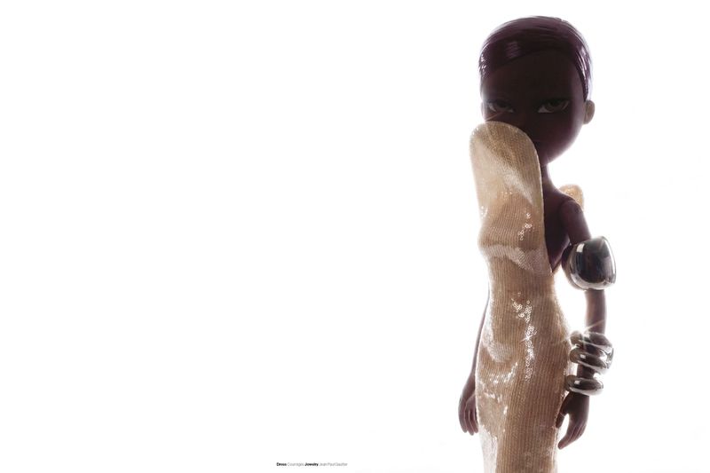 Bratz doll wearing a sculpted gold sequin gown with chunky silver arm cuffs against an illuminated white background.