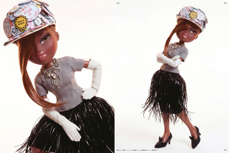 Styled Bratz doll wearing a grey top, black fringe skirt, white gloves, crystal necklace, and badge-covered cap against white background.