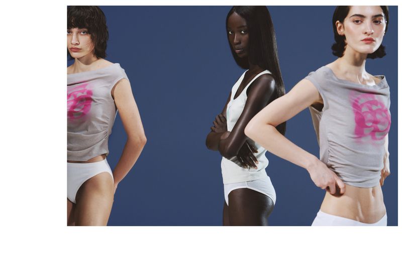 Three models pose in cropped grey graphic shirts and white underwear against a solid blue studio backdrop.