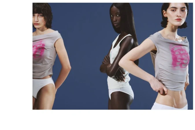 Three models pose in cropped grey graphic shirts and white underwear against a solid blue studio backdrop.