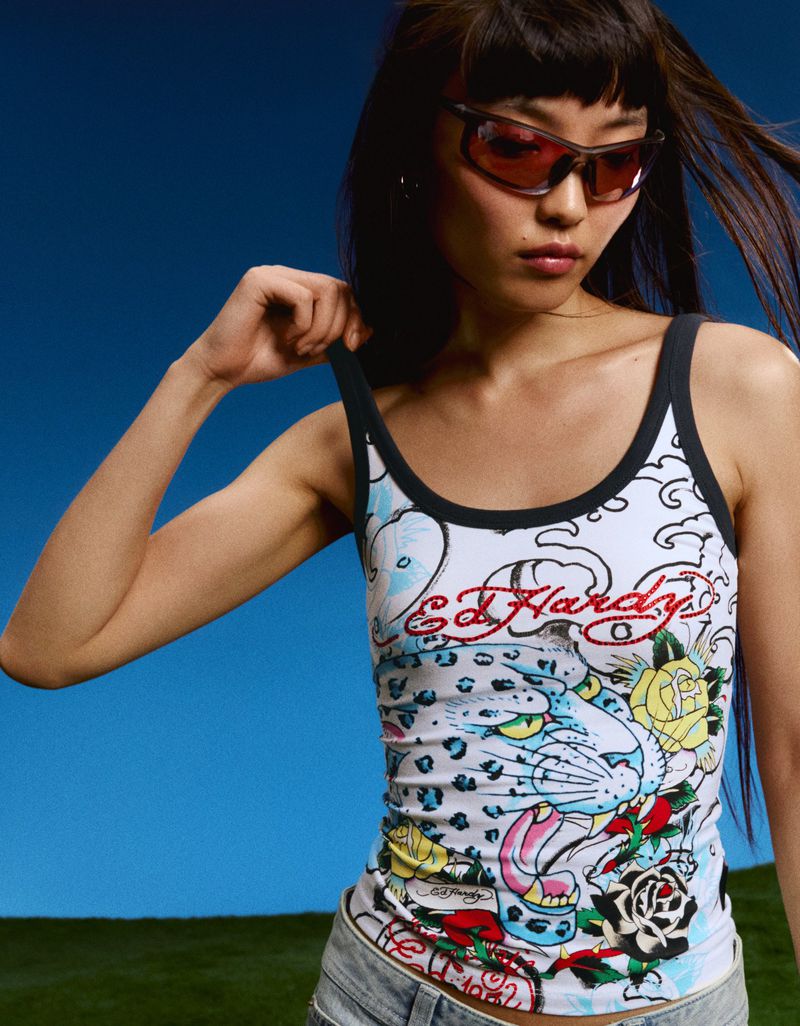 Model Lian Jia wearing tinted sunglasses and an Ed Hardy graphic print tank top against an open blue sky.