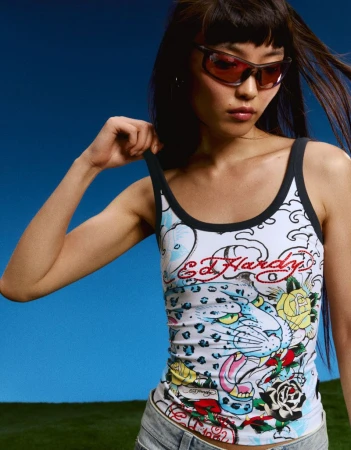Model Lian Jia wearing tinted sunglasses and an Ed Hardy graphic print tank top against an open blue sky.
