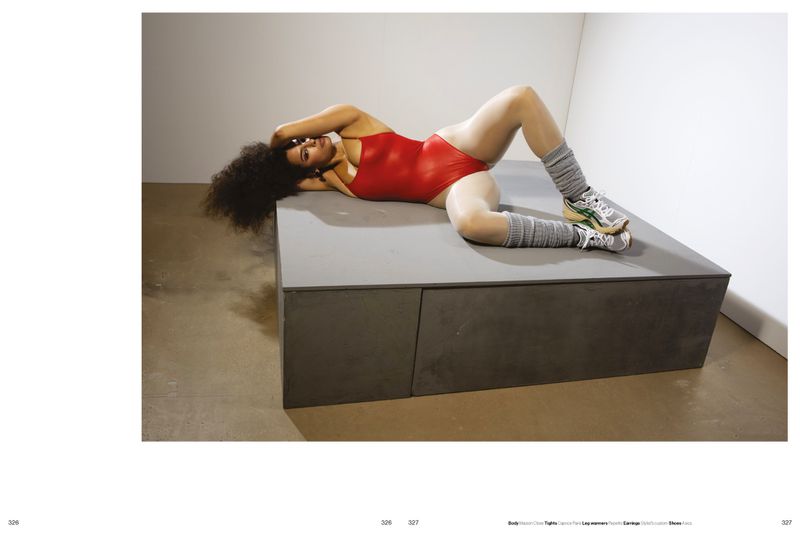 Model lying on a raised grey platform wearing a red bodysuit and grey leg warmers