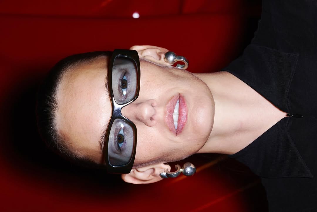 Close-up studio shot of a model wearing glasses and silver earrings against a red backdrop, emphasizing beauty and modern fashion.