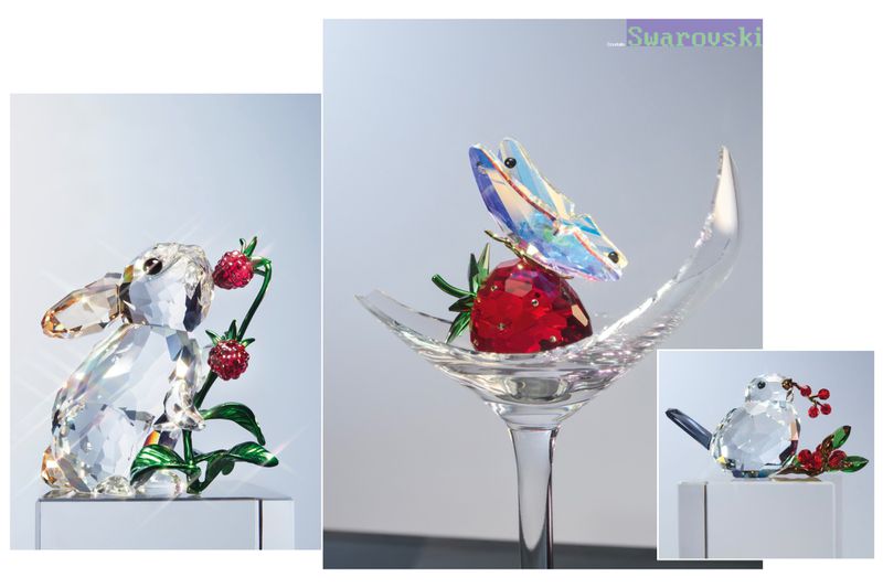 Editorial still life of crystal figurines including a rabbit, bird, and strawberry with butterfly resting in a broken glass.