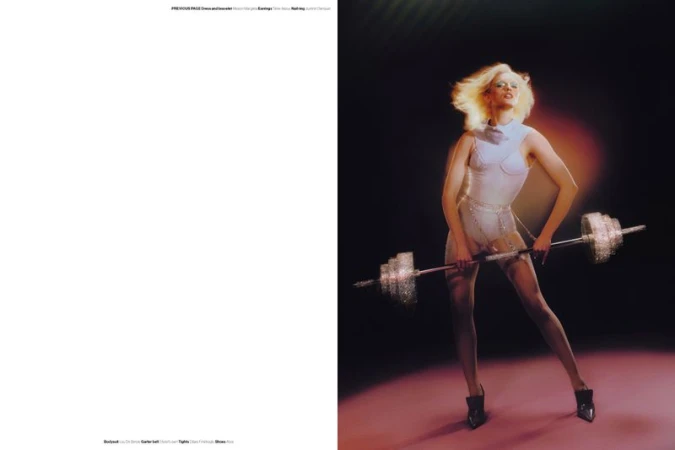Model Fran Summers wearing a white bodysuit while holding a crystal barbell in a dark studio editorial spread.
