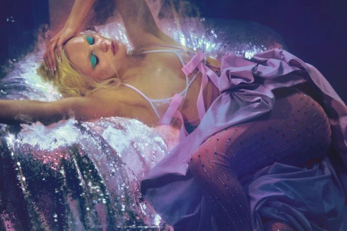 Model Fran Summers reclining on a shimmering sequined surface wearing a lilac gown and vibrant blue eyeshadow.