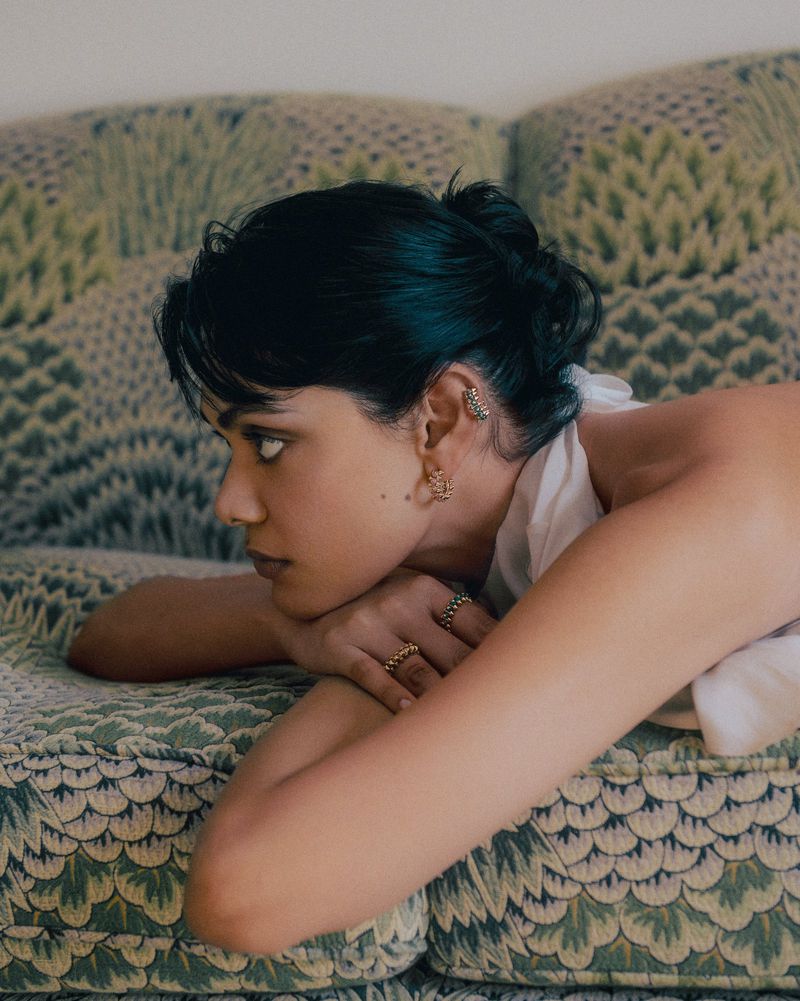 Close-up profile of a woman resting her chin on her crossed arms while lying on a green patterned upholstered sofa.