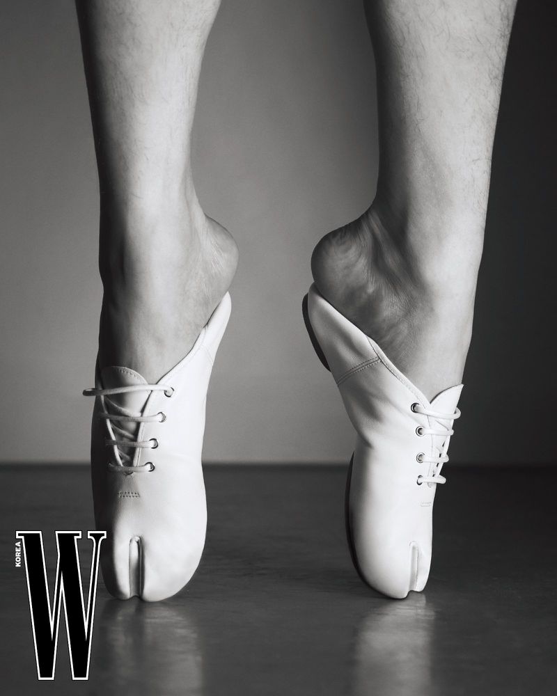 Close-up of bare legs and arched feet in white lace-up split-toe tabi shoes standing on tiptoes in black and white.