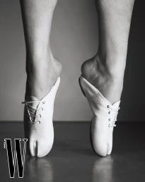 Close-up of bare legs and arched feet in white lace-up split-toe tabi shoes standing on tiptoes in black and white.