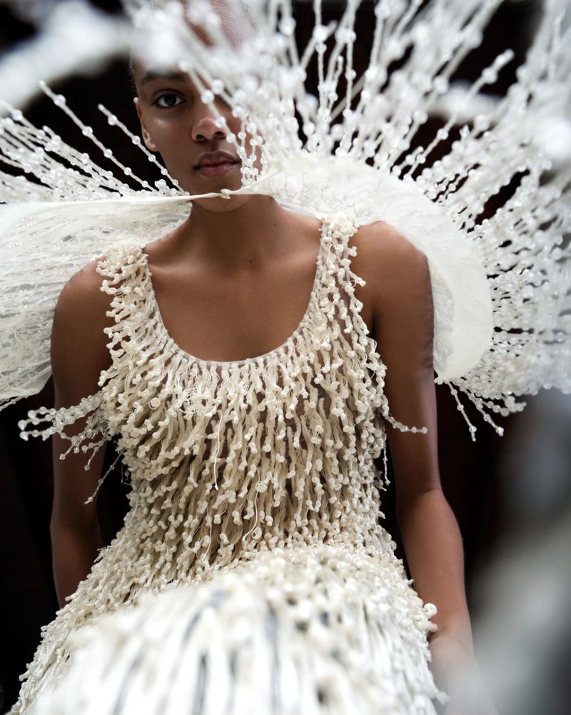 Model wearing a textured white fringed dress and elaborate beaded headpiece in a beauty projects issue editorial portrait.