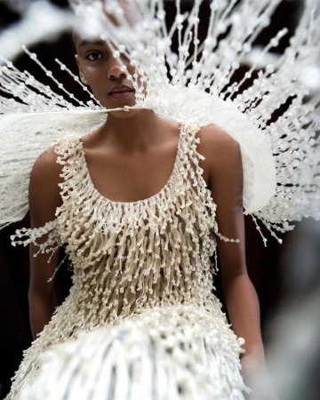 Model wearing a textured white fringed dress and elaborate beaded headpiece in a beauty projects issue editorial portrait.