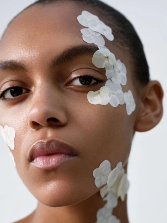 Close-up portrait of model Bebe Parnell with delicate white flower petals applied across her temple, cheek, and neck.