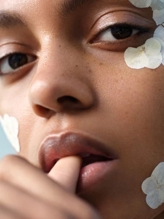 Close-up beauty portrait of a model with white flower petals on her skin, touching her lips.