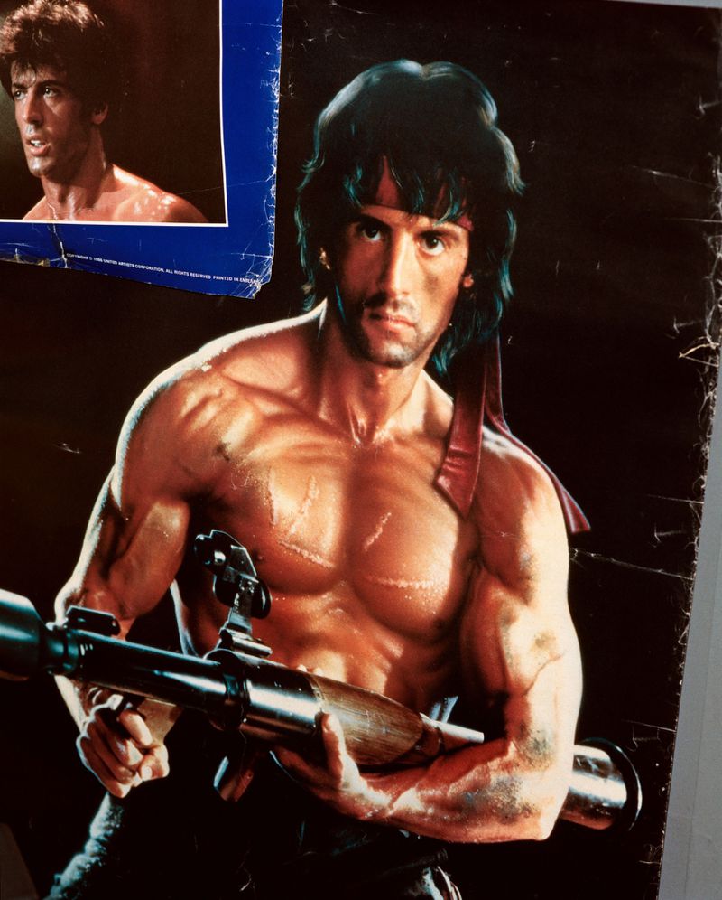 Vintage poster of shirtless Sylvester Stallone as John Rambo holding a rocket launcher with a red headband.