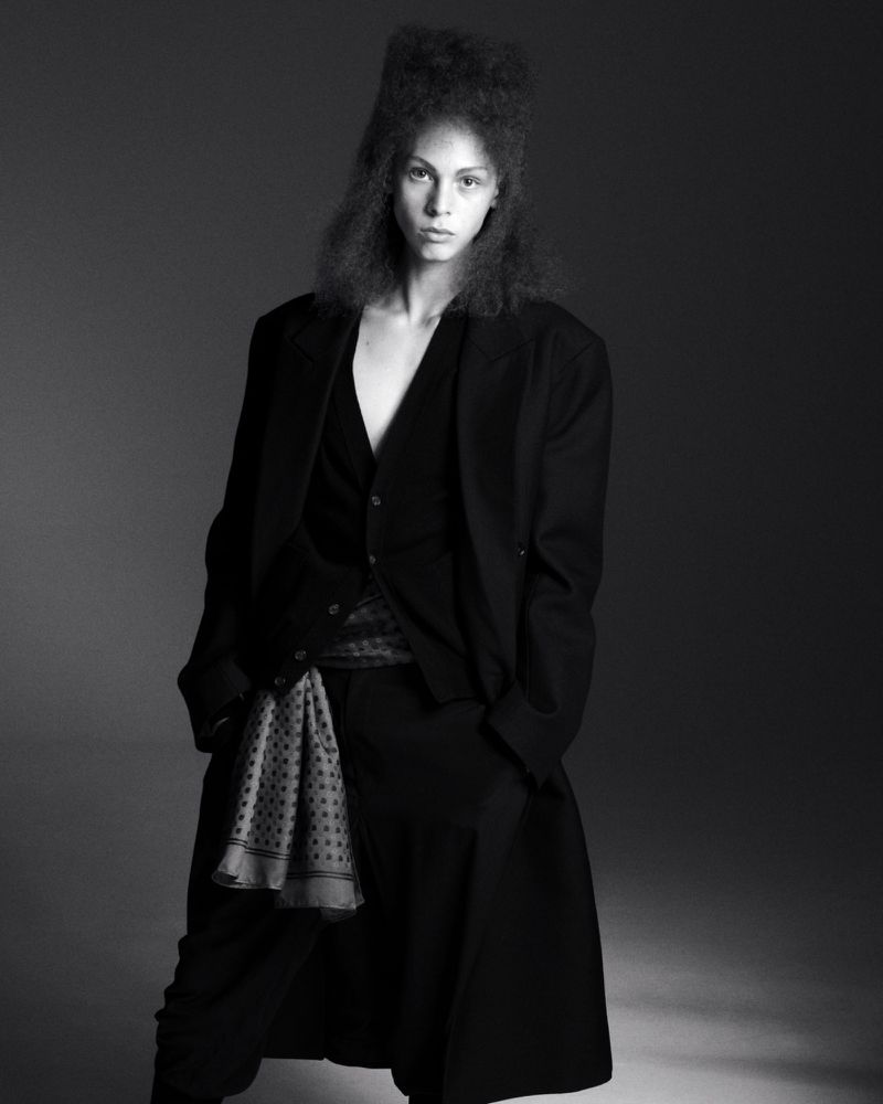 Model in black suit and patterned scarf against a dark studio background