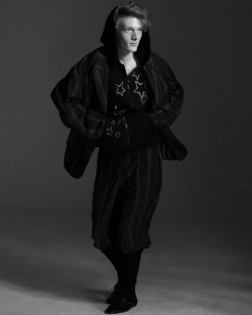 Black and white editorial portrait of Nik Dermendzhiev wearing a star-patterned hoodie and jacket for Arena Homme +
