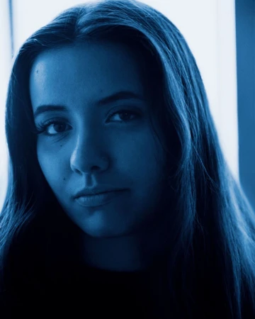 Blue-toned close-up portrait of a young woman with long dark hair looking directly at the camera.