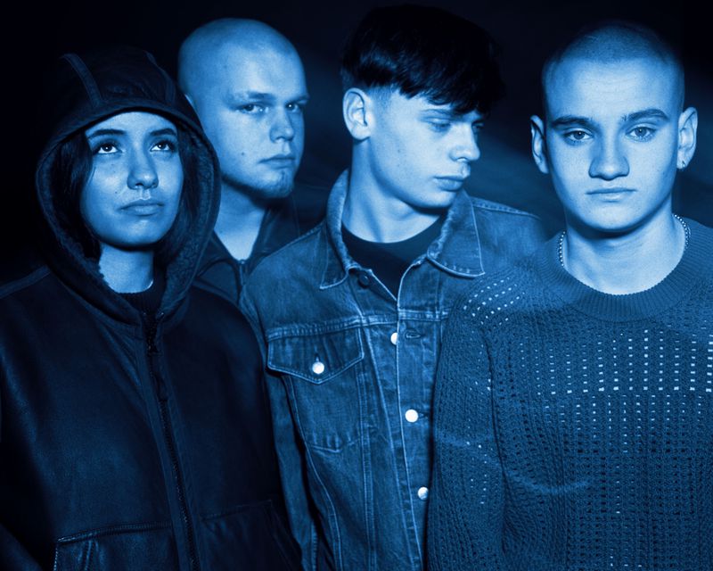 Group portrait of four young people bathed in blue light wearing a denim jacket, hooded coat, and textured knit sweater.