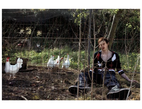 Model Joe Bottomer seated on the grass beside a wire mesh enclosure with white chickens in an outdoor rural setting.