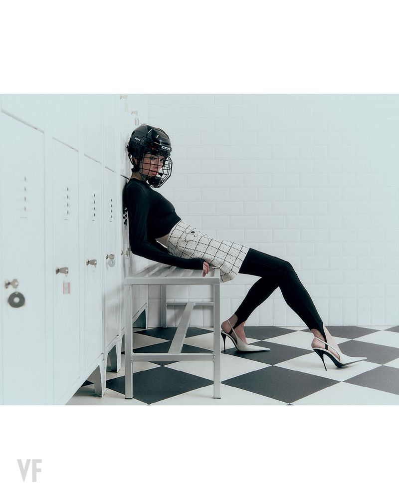 Model wearing hockey helmet and black top sitting on bench against lockers in Vanity Fair Italia editorial
