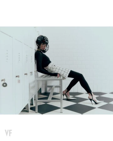 Model wearing hockey helmet and black top sitting on bench against lockers in Vanity Fair Italia editorial