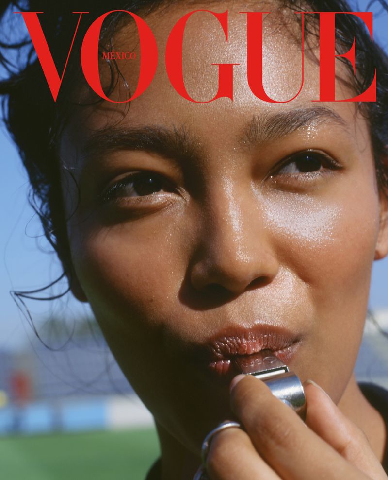 Close-up portrait of a woman with dark hair and shiny skin, wearing ring, with a whistle in her mouth, Vogue magazine cover